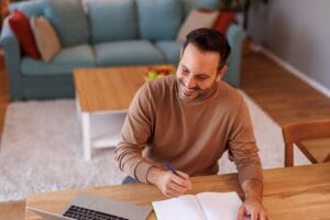 high angle view male entrepreneur using laptop writing note pad while working home office